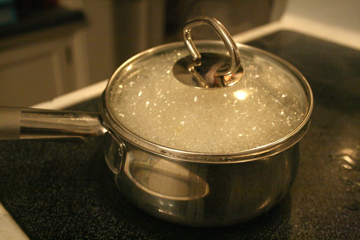 A lidded steel pot boiling water on a dark cooktop.