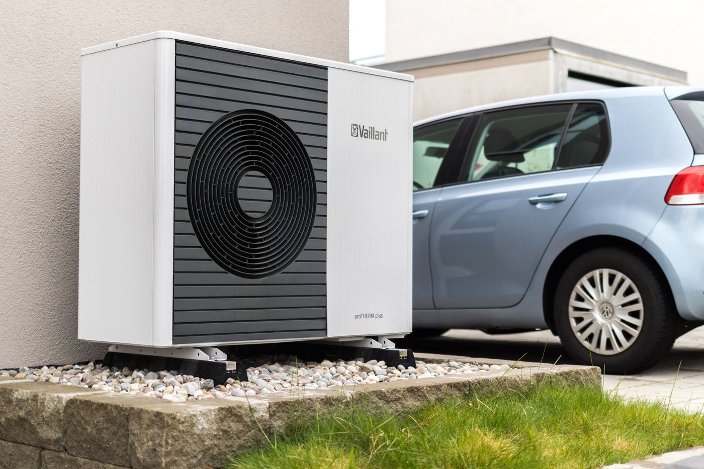 A Vaillant air source heat pump outdoor unit mounted against a house wall next to a parked car, illustrating the type of natural-refrigerant heat pump technology Bosch is bringing to its own lineup.