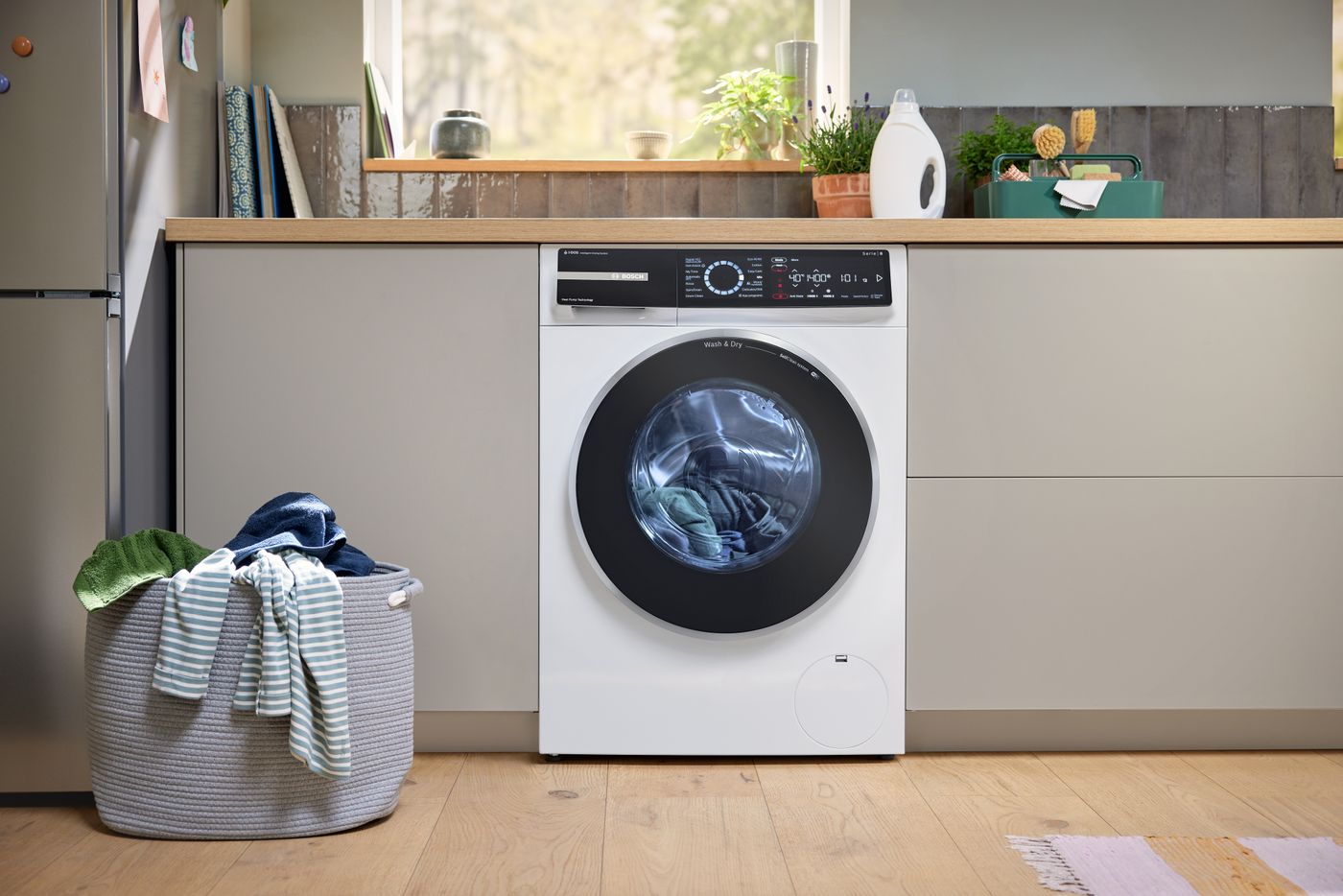Bosch Series 8 heat pump washer-dryer installed under a kitchen counter next to a laundry basket