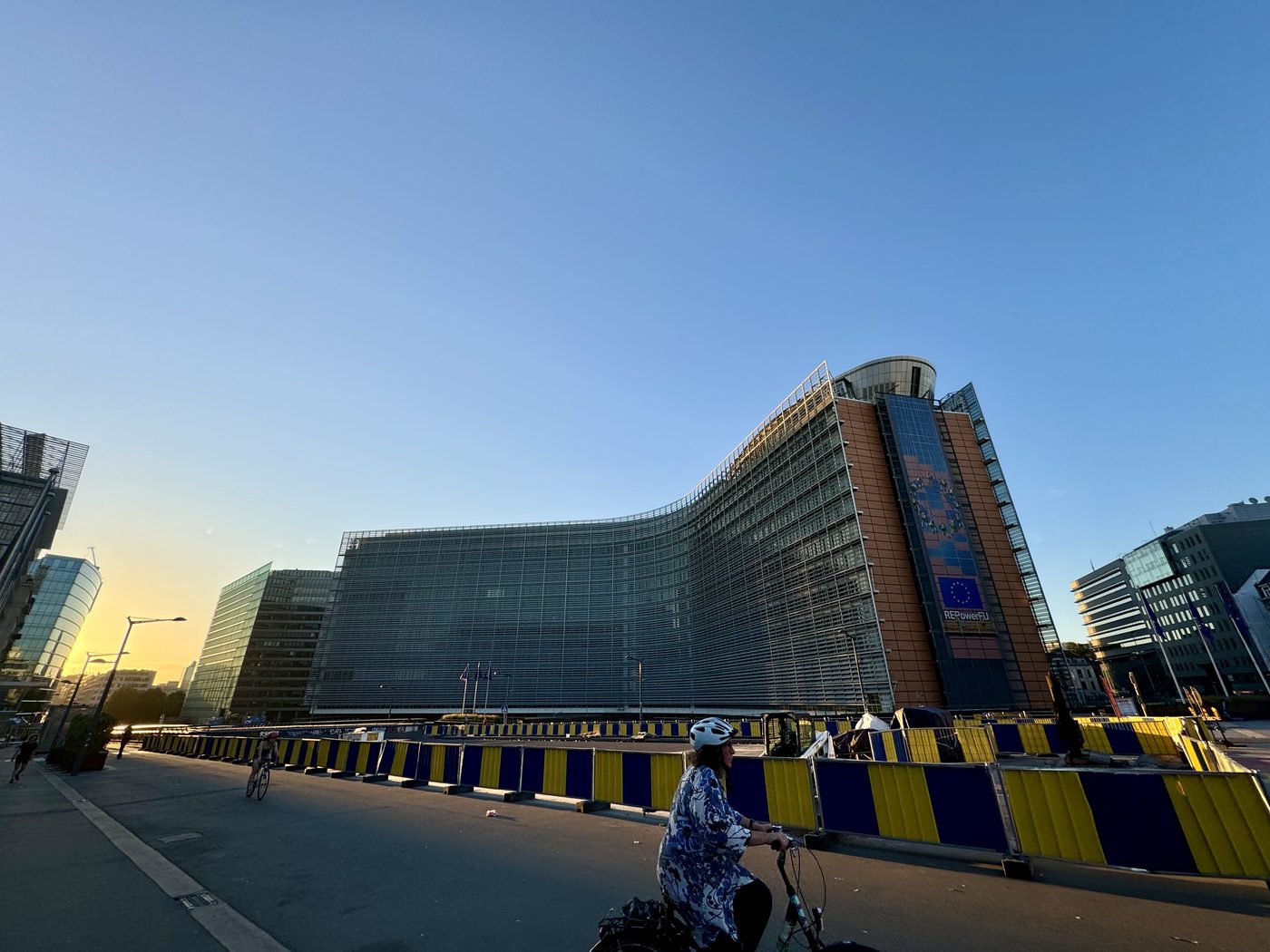 The Berlaymont building, European Commission headquarters in Brussels, at sunrise with an EU flag and REPowerEU banner visible.