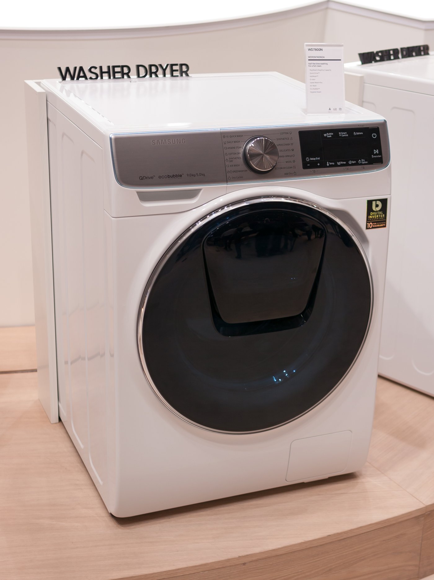 A white Samsung front-load washer dryer on display, showing its control panel and drum door.